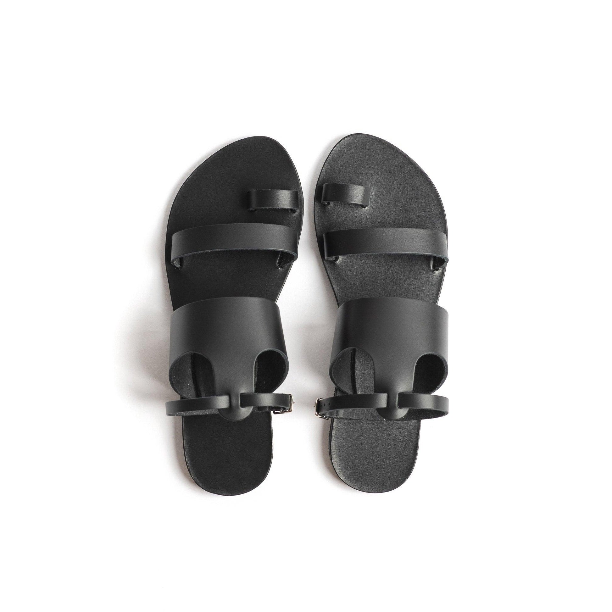 Top view of black flats with ankle strap against a white background.