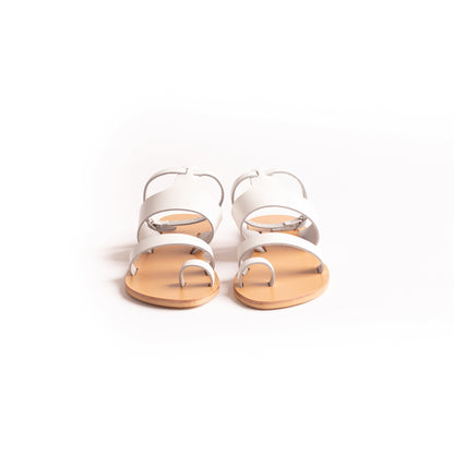 Front view of white flat sandals against a white background. They are white ankle strap sandals.