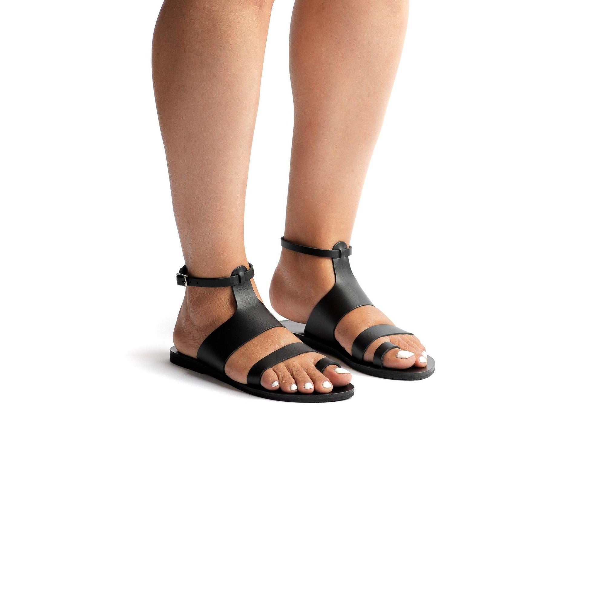 Woman wearing black flats with ankle strap against a white background.