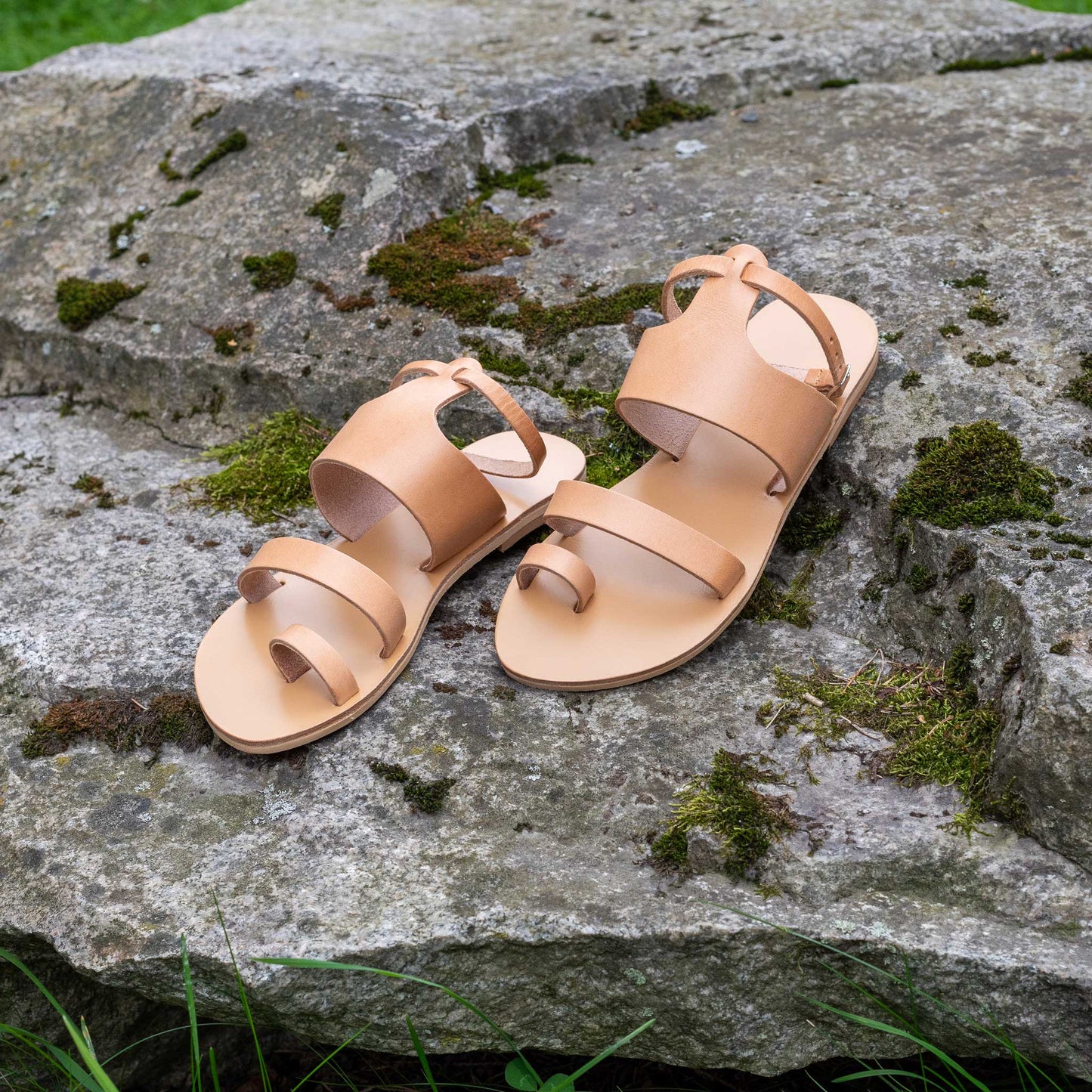 Tan flat sandals with strap for woman on a rock. They are flat sandals with ankle strap.