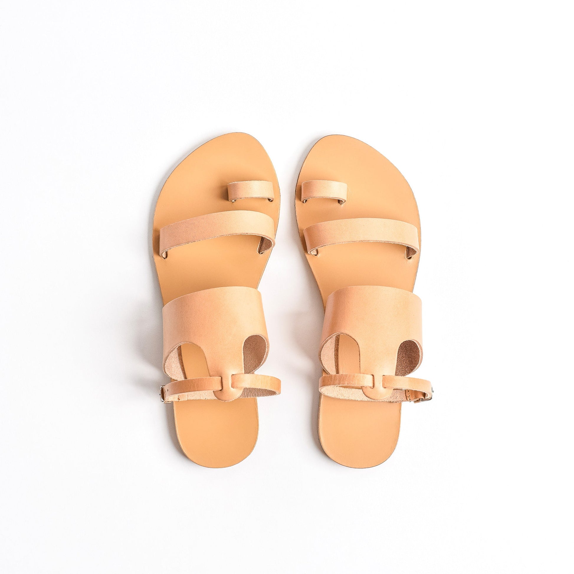 Top view of tan flat sandals with strap for women against a white background. They are flat sandals with ankle strap.