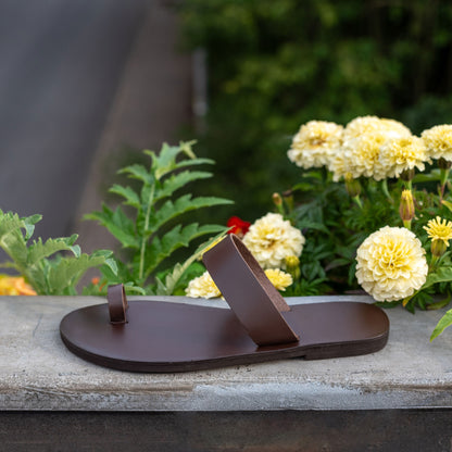 Astara leather sandals women's on a bench surrounded by flowers. They are flat sandals brown.