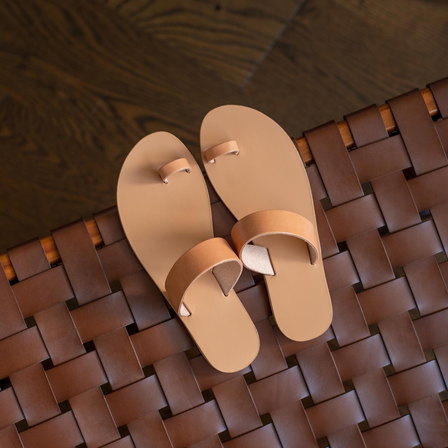 Top view of elegant flat sandals in camel on a weaved leather chair. Part of our flat footwear for womens collection.