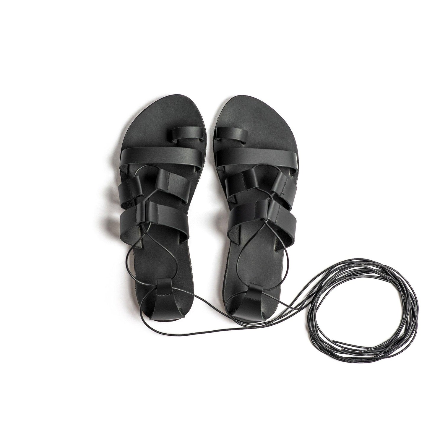 Top view of Athanasia black strappy flats on a white back. They are flat sandals lace up.