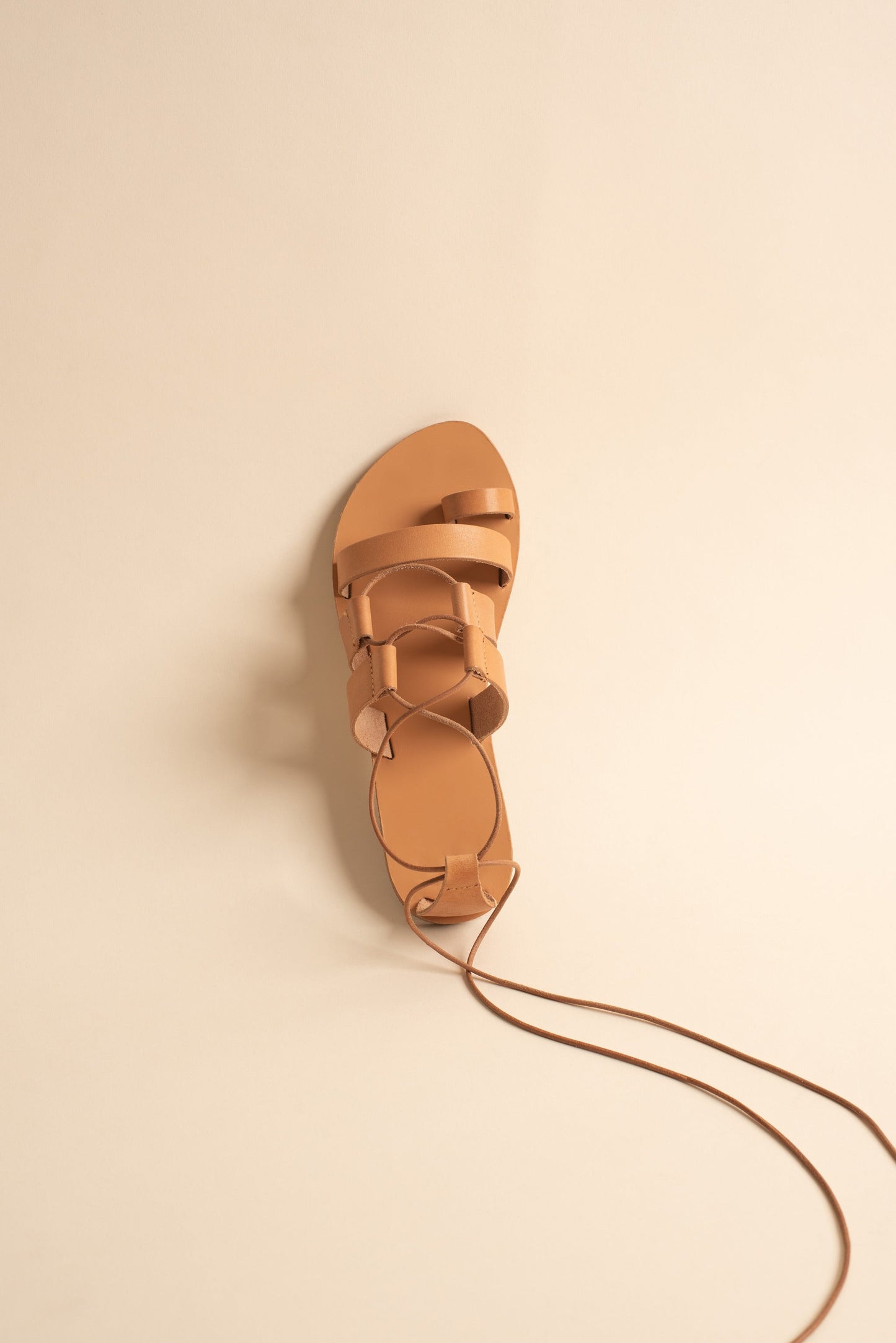 Athanasia flat sandals strappy in tan against a beige background. They are women's lace up flats.