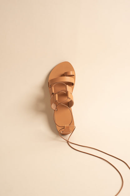 Athanasia flat sandals strappy in tan against a beige background. They are women's lace up flats.