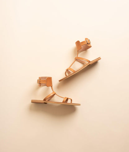 Athena leather flat sandals in tan against a beige background. These tan sandals flat are flat sandals buckle.