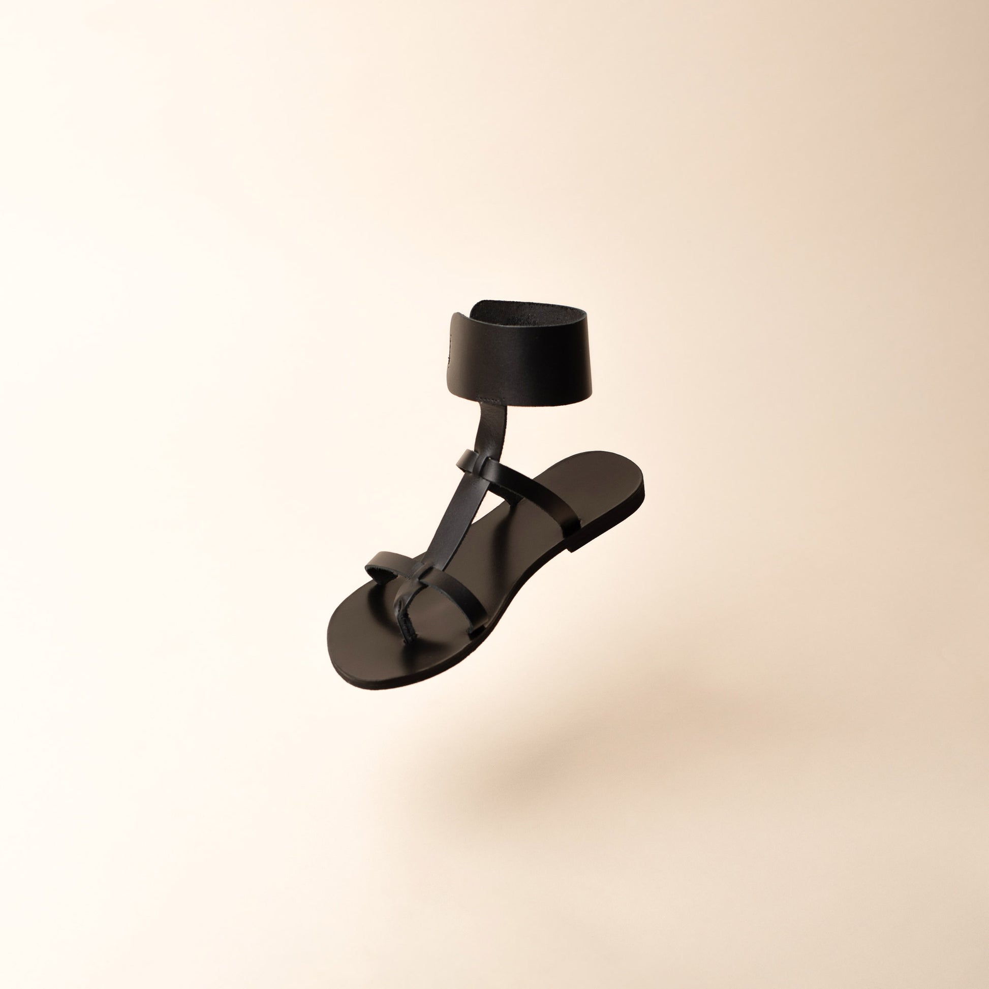 Black leather flats floating against a beige background. These black leather sandals are black flat gladiator sandals.
