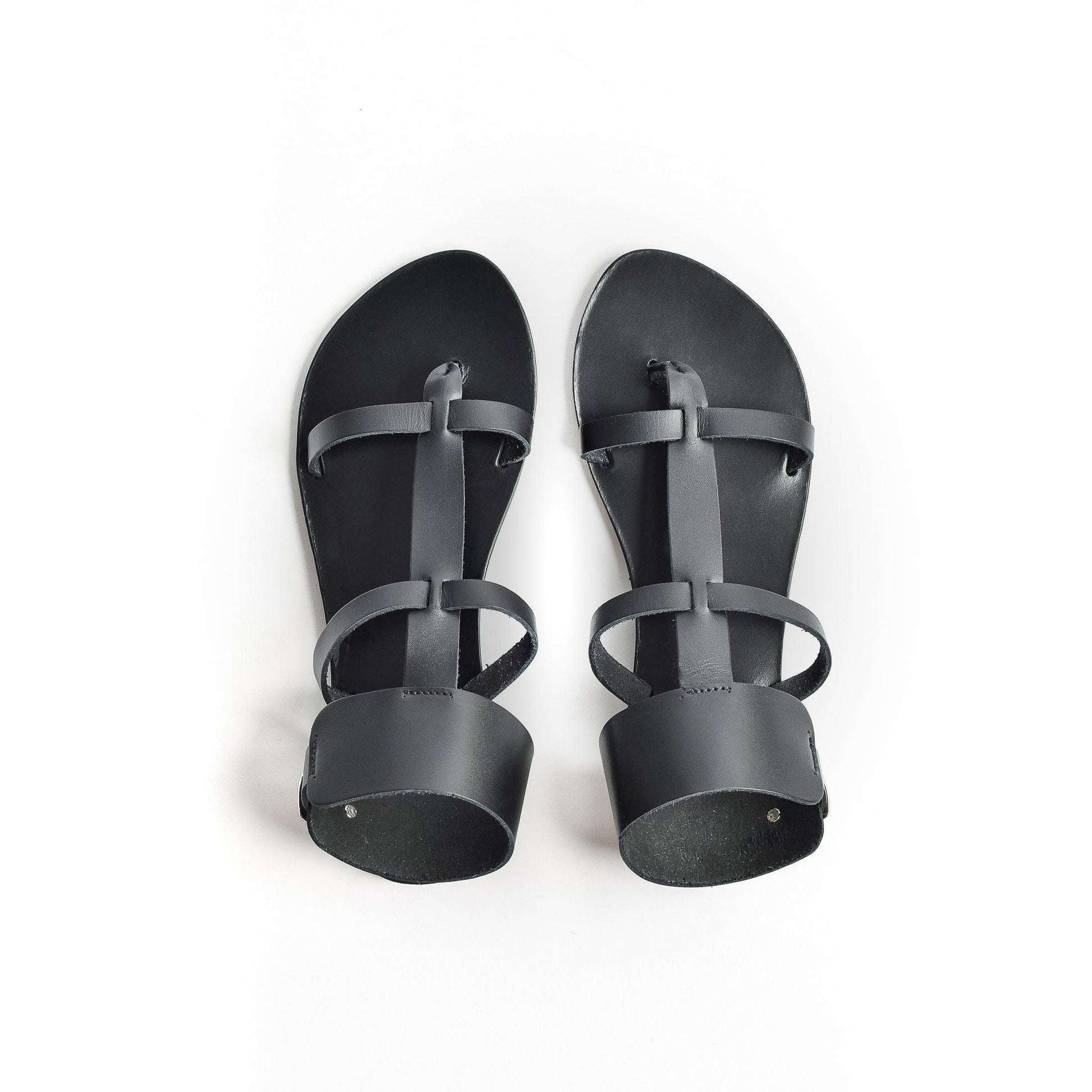 Top view of black leather sandals against a white background. They are black flat gladiator sandals.