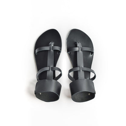 Top view of black leather sandals against a white background. They are black flat gladiator sandals.