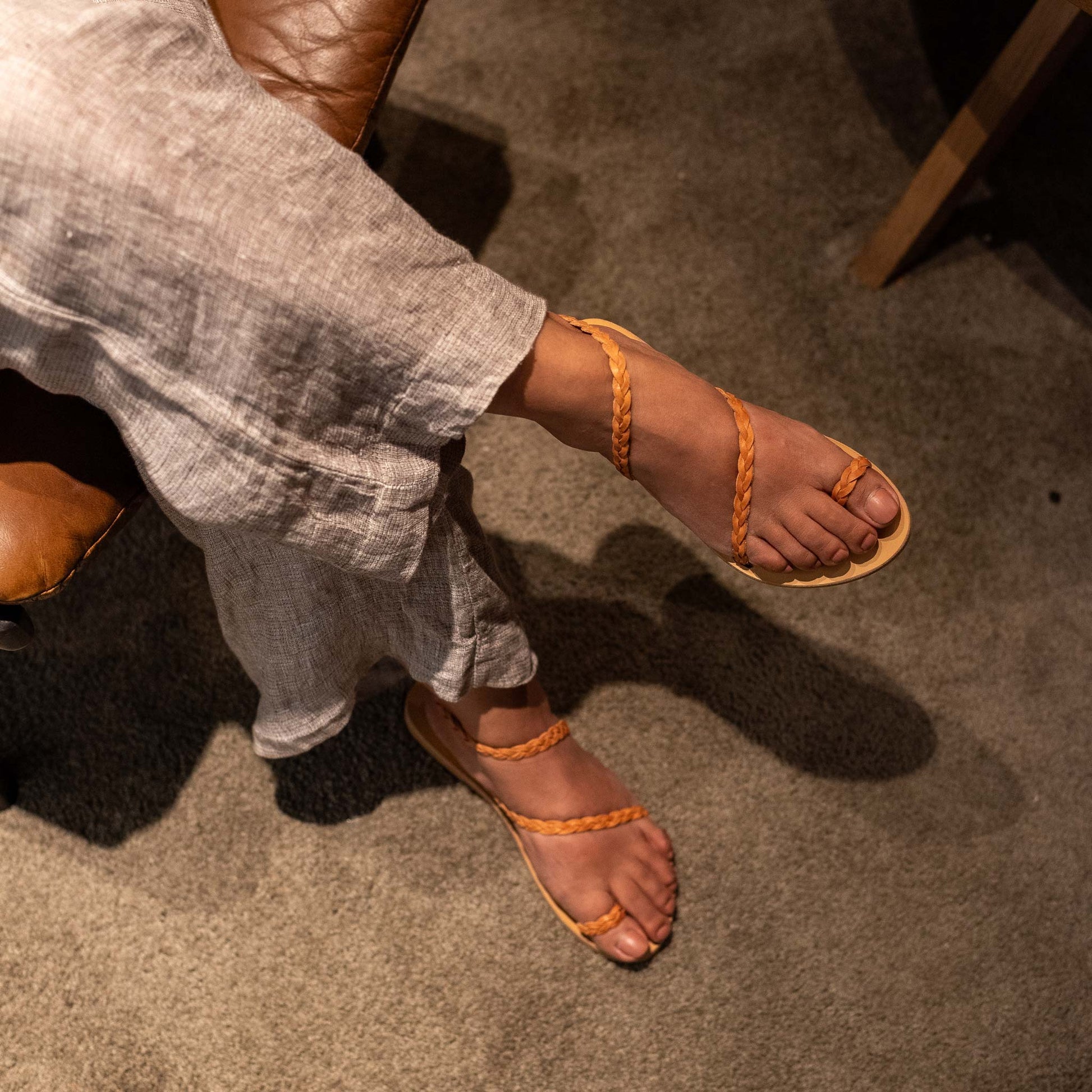 Woman wearing tan sandals for women flat on a carpeted floor. They are flat sandals with back strap.