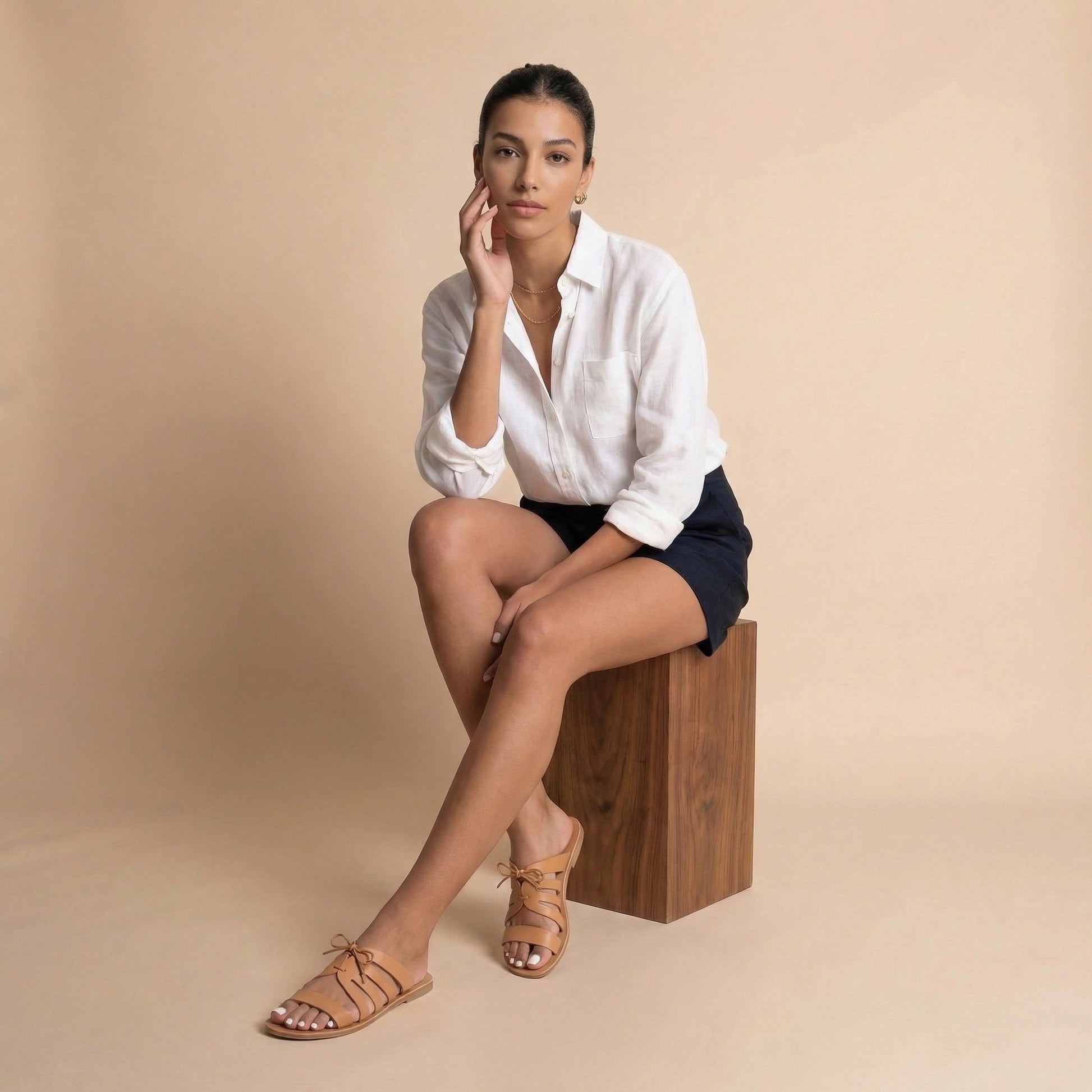 Woman wearing a pair of tan comfortable flats against a beige background. They are a pair of bow sandals flat.
