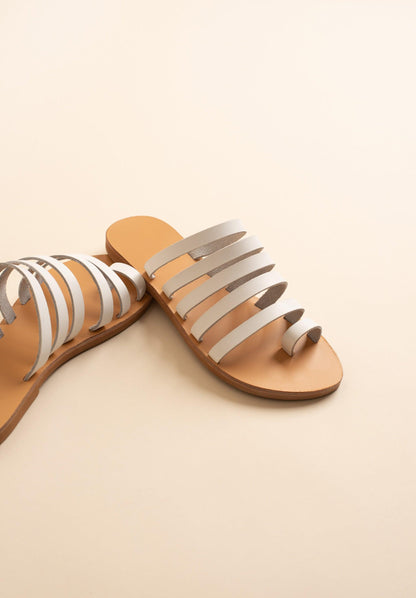 Harmonia white slide sandals against a beige background. These white leather sandals are white flats for women.
