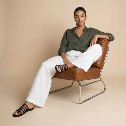 Woman wearing Harmonia womens leather flats in black against a beige background. They are step in sandals flat.