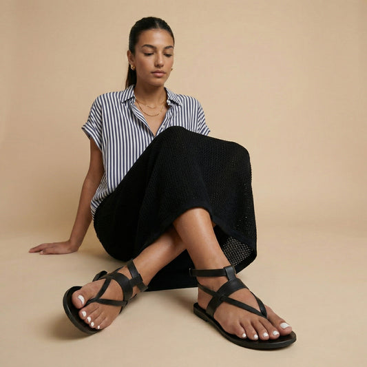 Woman wearing Rhea double dtrap sandals in black with blue cropped jeans against a beige background. They are black flats for women.