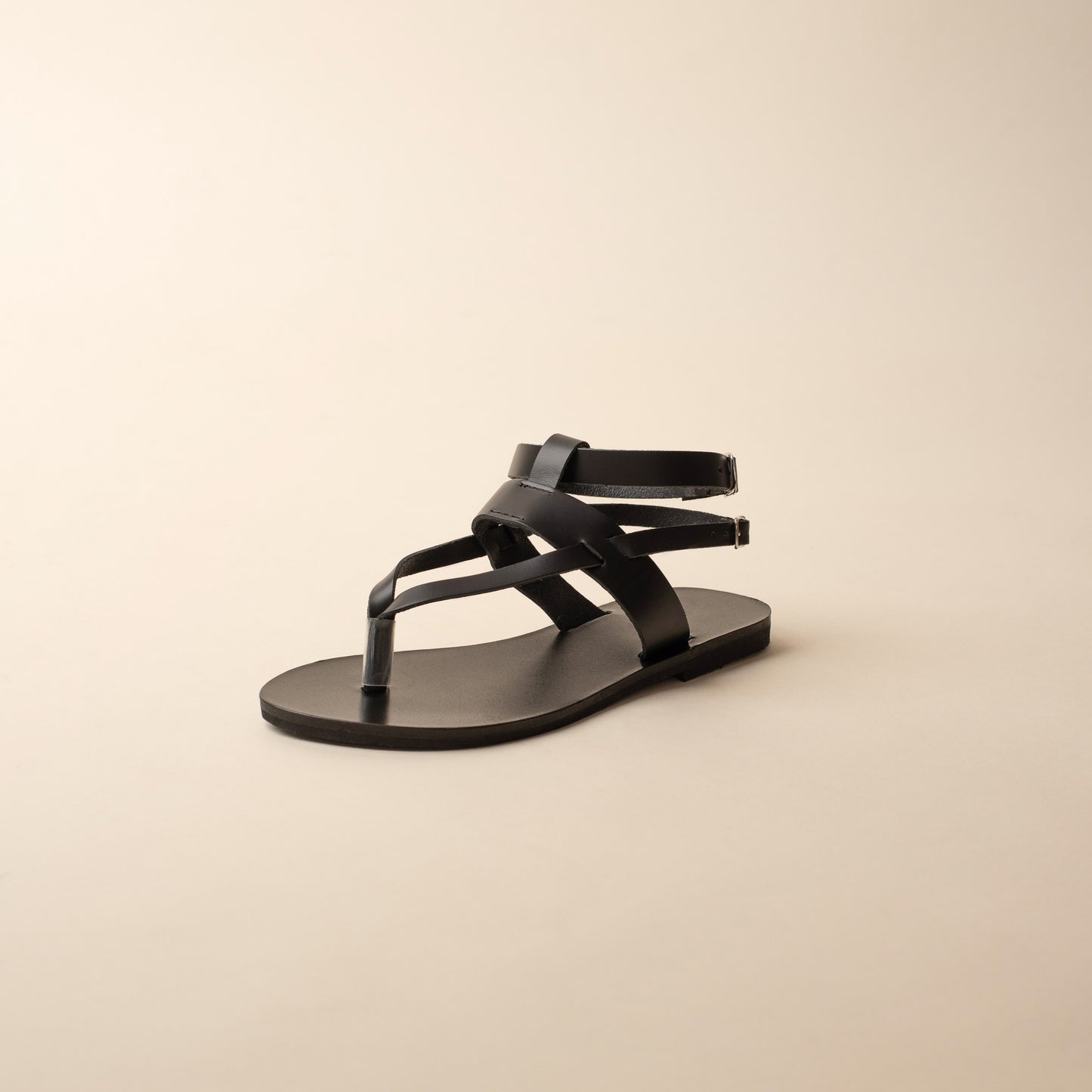 A single sandals of Rhea black flats for women on a beige background.