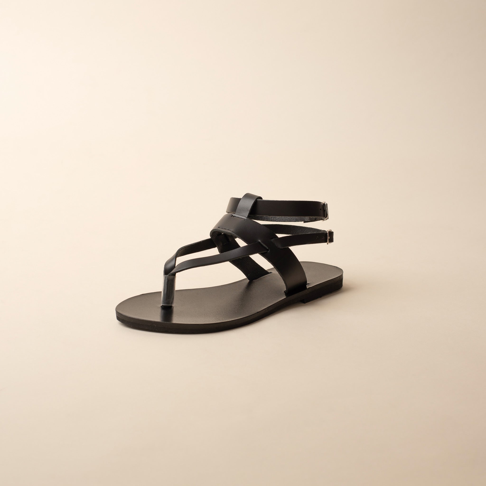 A single sandals of Rhea black flats for women on a beige background.