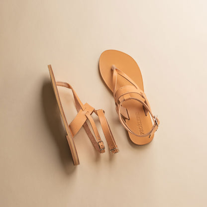 Top view of a pair of tan flat sandals designer on a beige background. They are women's flats with ankle straps.