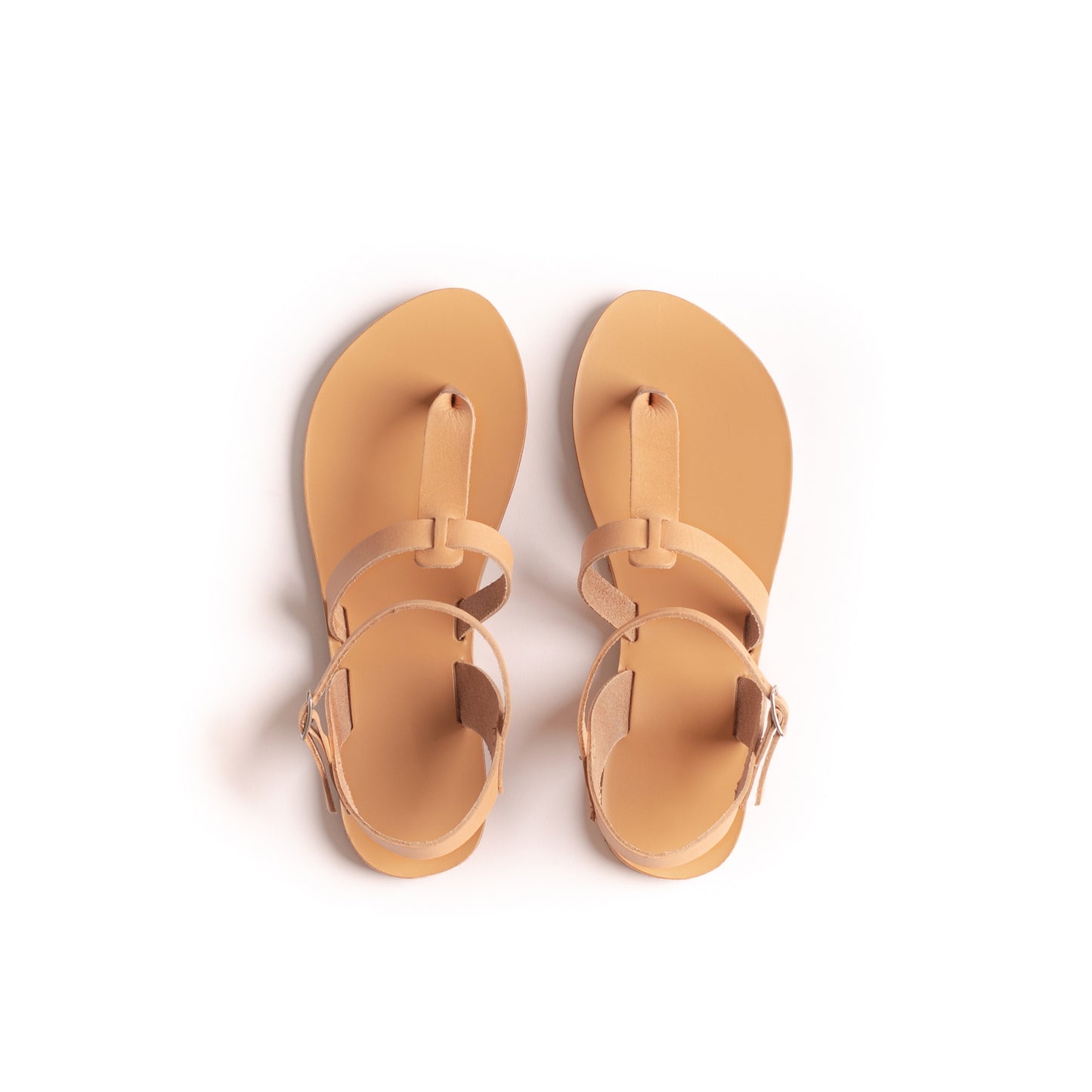 Top view of a pair of tan flat sandals one strap on a white background. They are flat sandals beige.