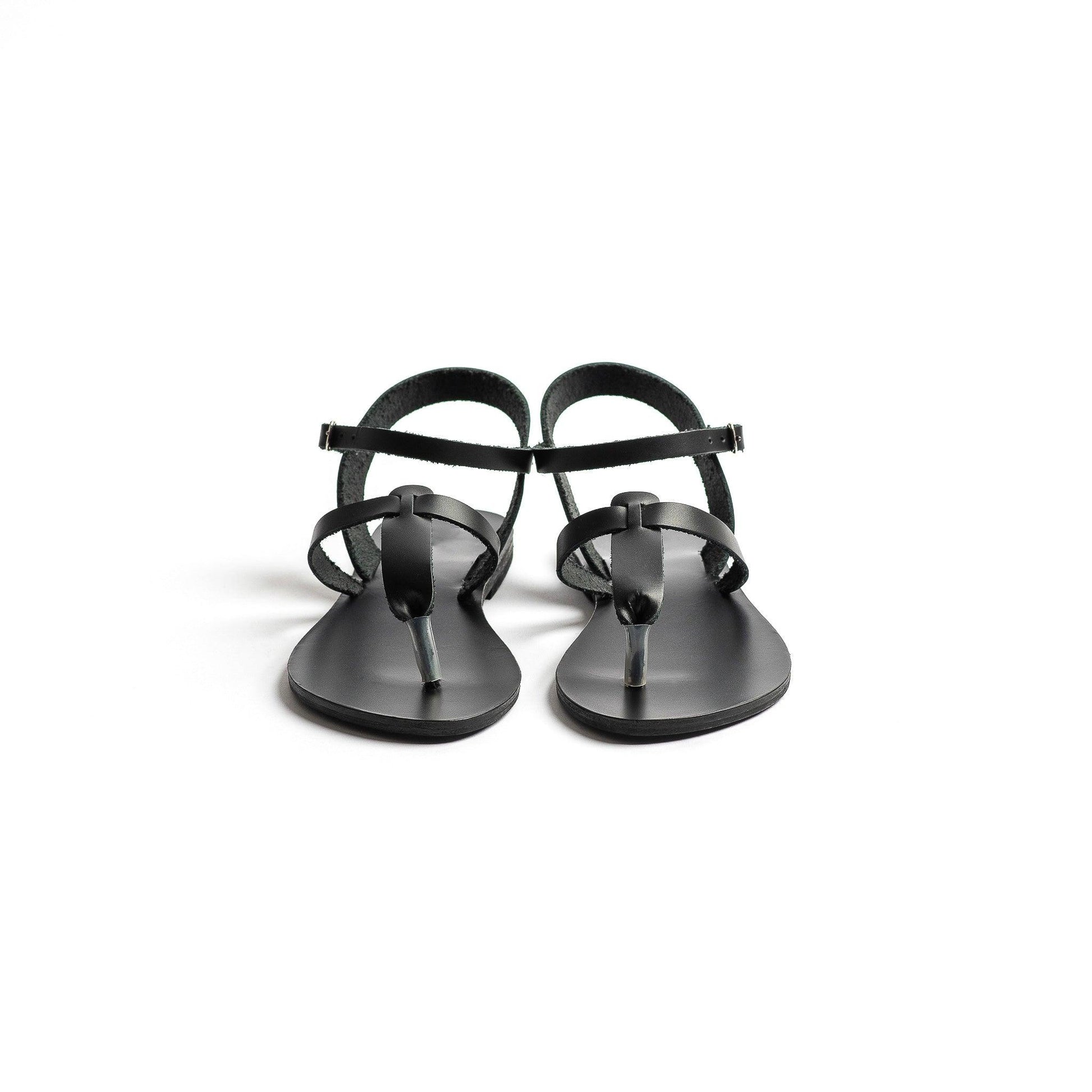Front view of a pair of black designer flat sandals ankle strap on a white background. They are flat sandals t strap.