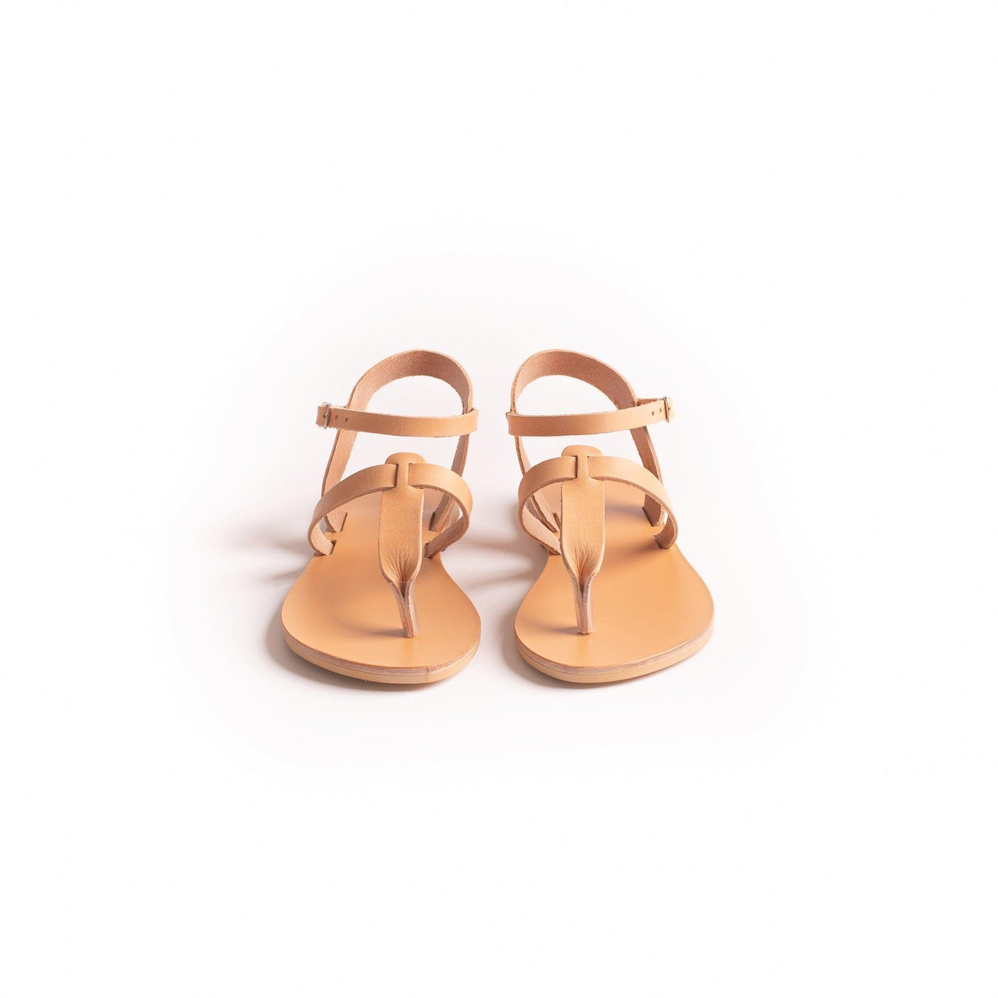 Front view of a pair of tan flat sandals one strap on a white background. They are flat sandals beige.