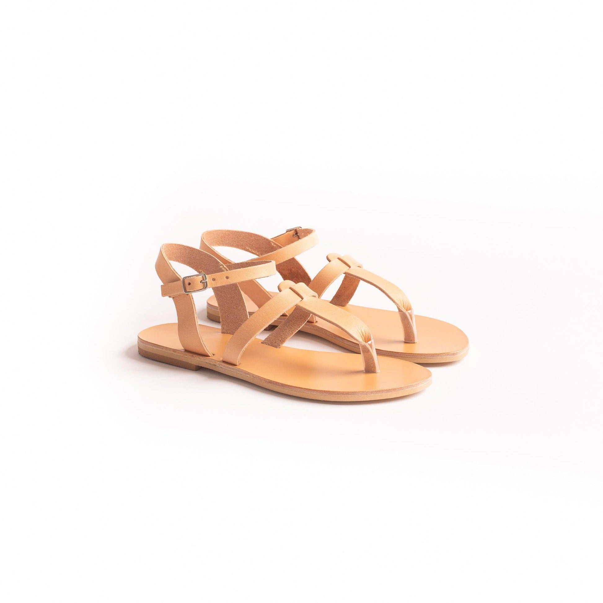 Pair of tan flat sandals t strap against a white background. They are flat sandals beige.