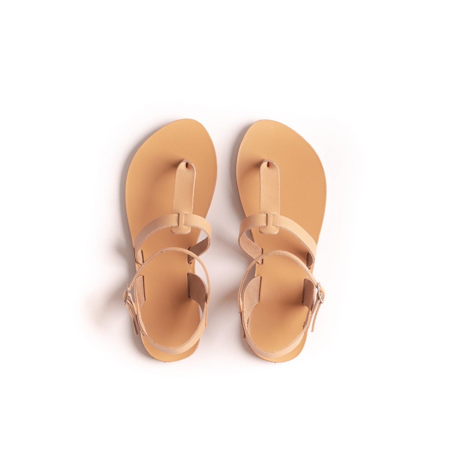 Top view of a pair of tan flat sandals one strap on a white background. They are flat sandals beige.