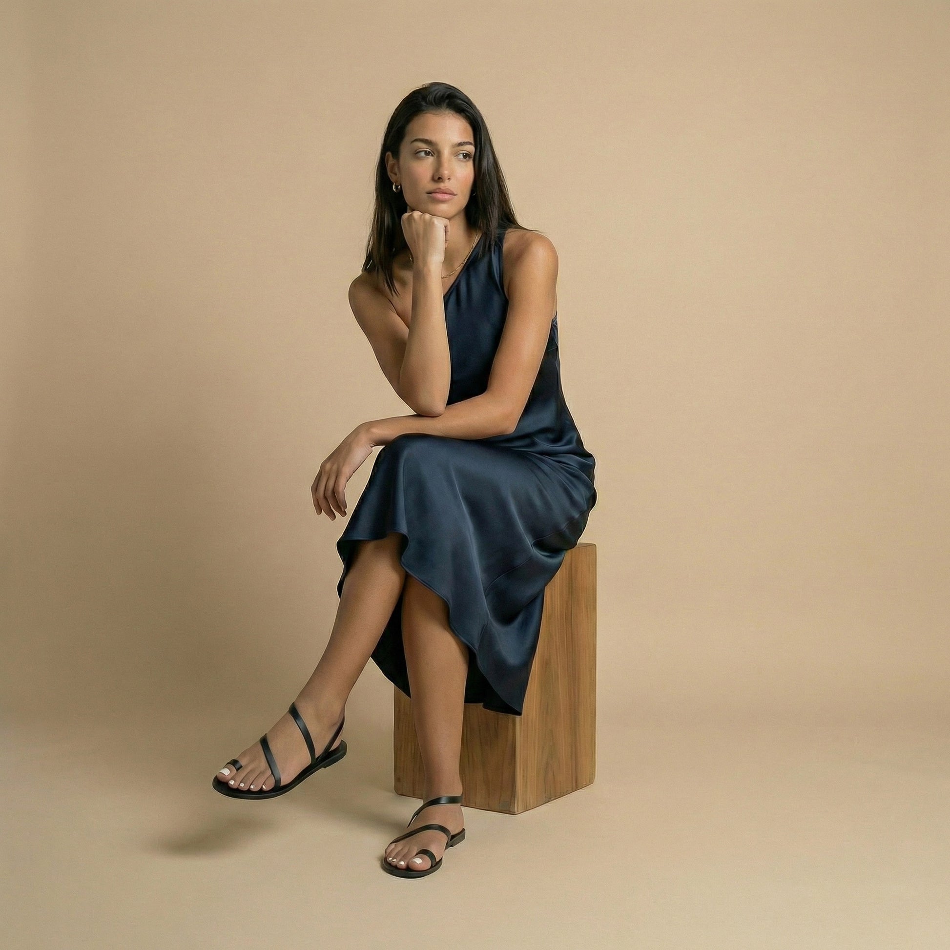 A woman wearing flat sandals black next to a potted plant with pink flowers on a stone pavement. They are fancy black flats.