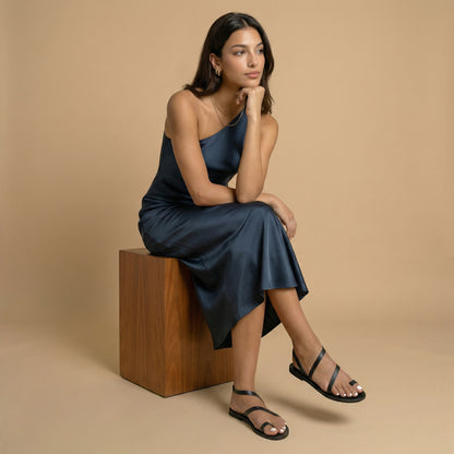 A woman wearing flat sandals black next to a potted plant with pink flowers on a stone pavement. They are fancy black flats.